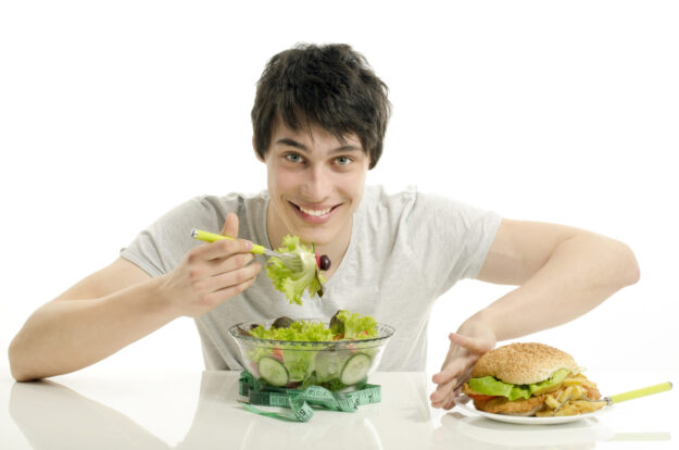 Healthy Eating Young man eating salad and pushing away a burger.